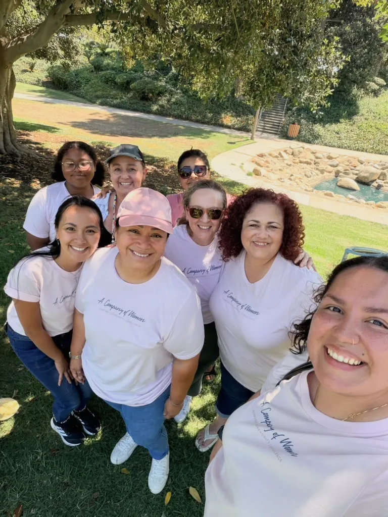 Women of A Company of Women smiling together outdoors in matching pink COW shirts